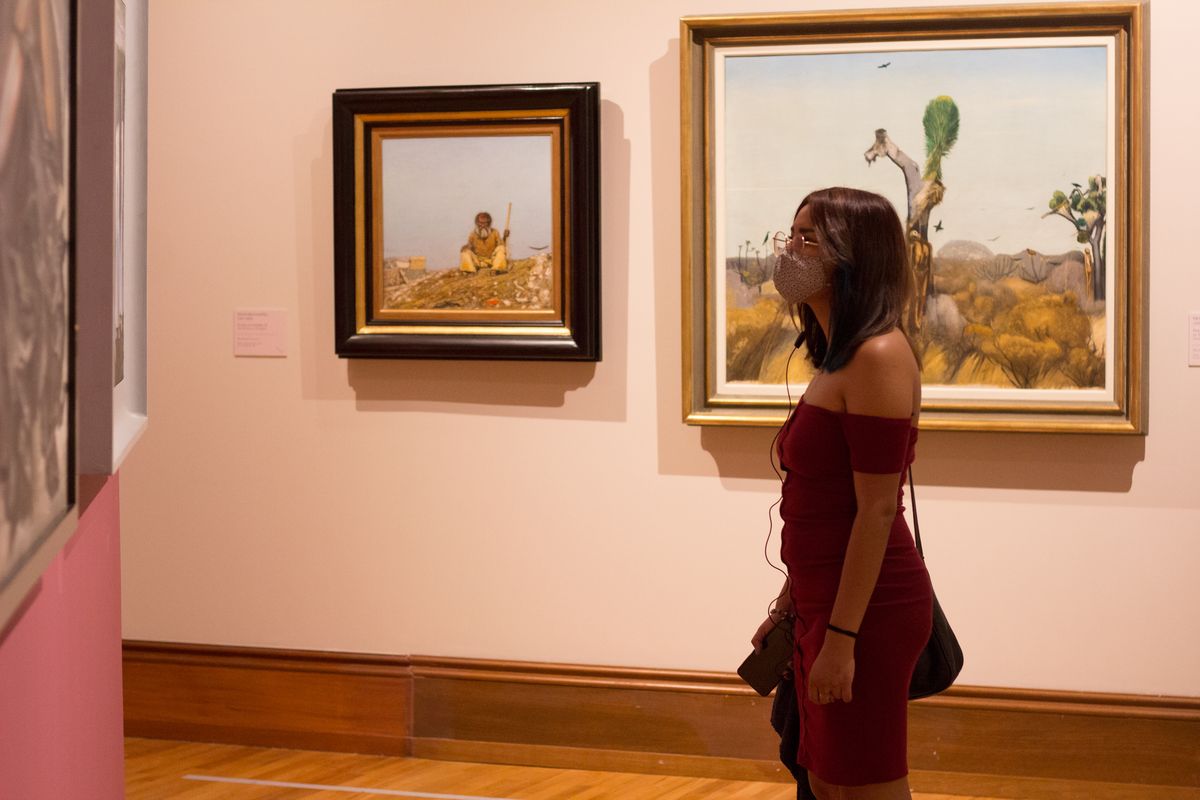una donna che indossa una maschera facciale si trova all'interno di un museo d'arte guardando un dipinto