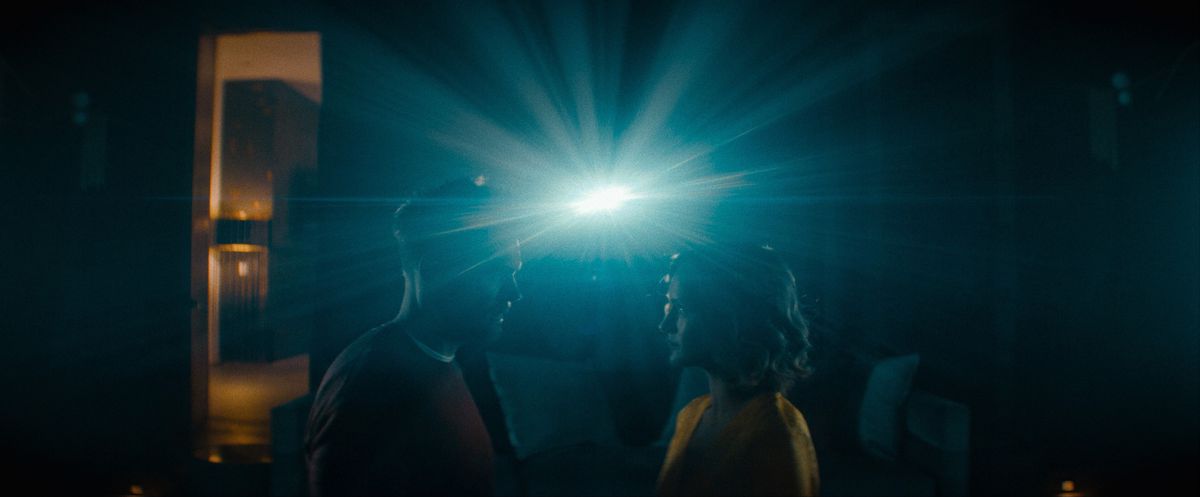 Joel McHale e Kerry Bishé si affrontano in una stanza buia con un'unica luce molto brillante alle spalle come un proiettore cinematografico