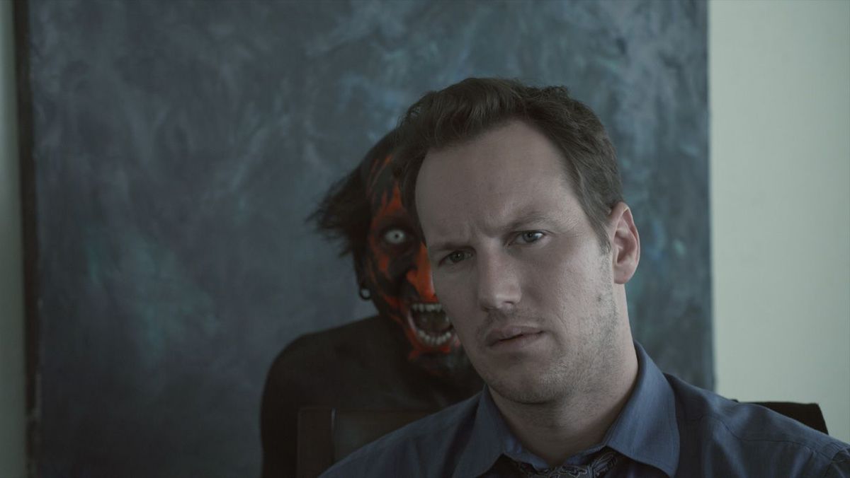Un demone dalla faccia rossa si acciglia di scherno dietro le spalle di Josh Lambert (Patrick Wilson) in Insidious di James Wan