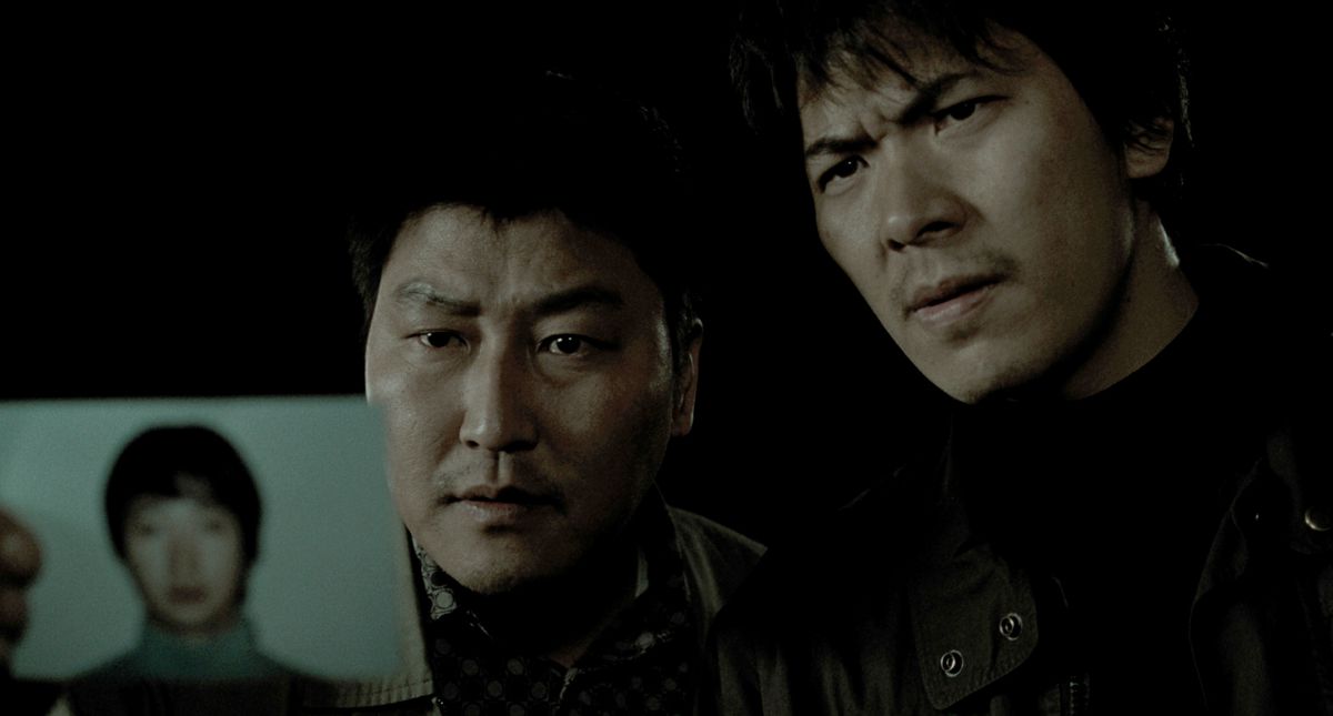 Il detective Park (Song Kang-ho) e Seo (Kim Sang-kyung) detengono la foto del sospettato di omicidio Park Hyeon-gyu (Park Hae-il) in Memories of Murder