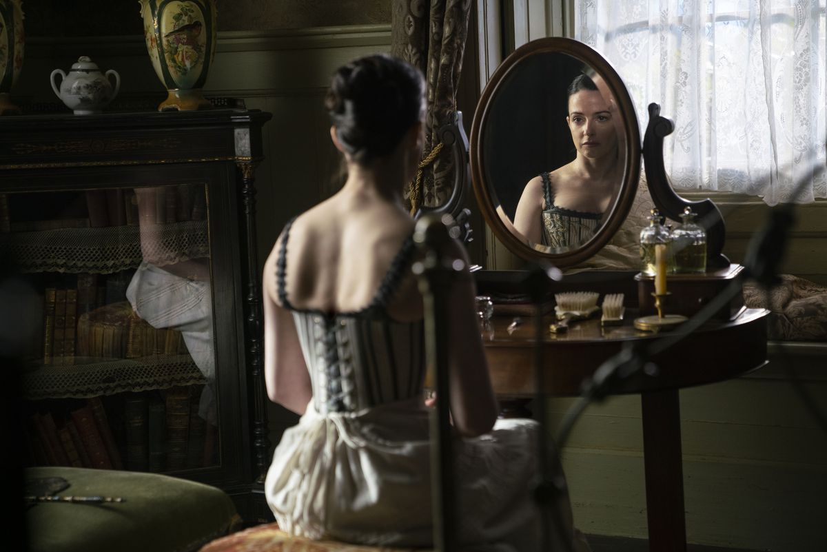 Laura Donnelly, in corsetto e sottogonna, si guarda allo specchio a Nevers