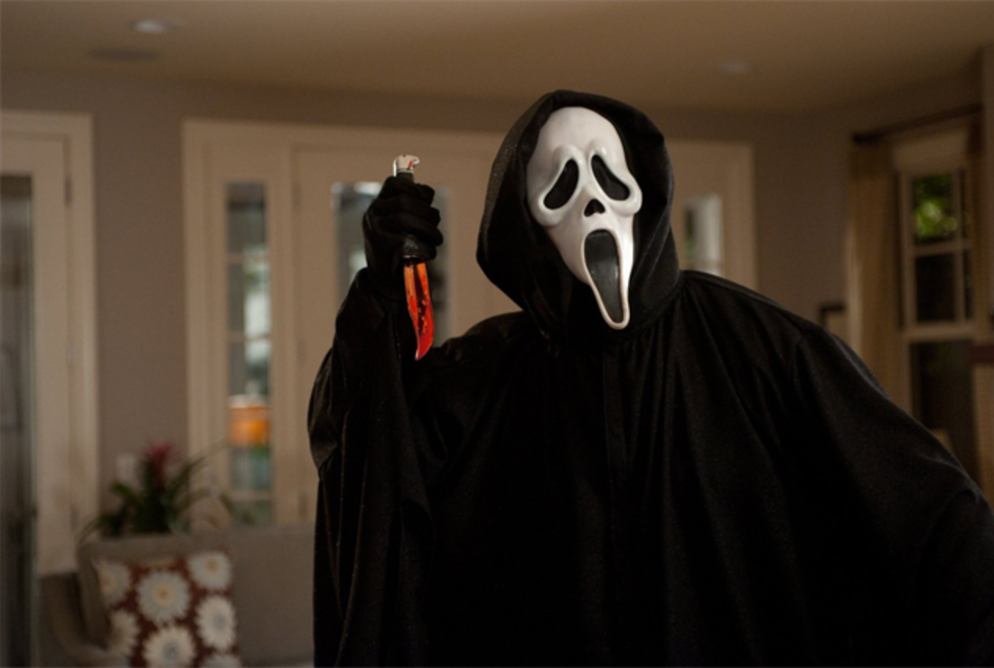 Un serial killer con una maschera macabra e un mantello nero usa un coltello coperto di sangue.