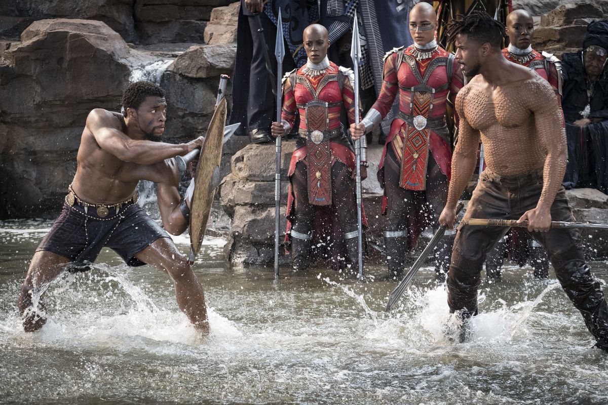 T'Challa/Black Panther (Chadwick Boseman) ed Erik Killmonger (Michael B. Jordan) combattono a torso nudo in acque profonde fino alle caviglie sullo sfondo degli osservatori di Dora Milaje in Black Panther del 2018