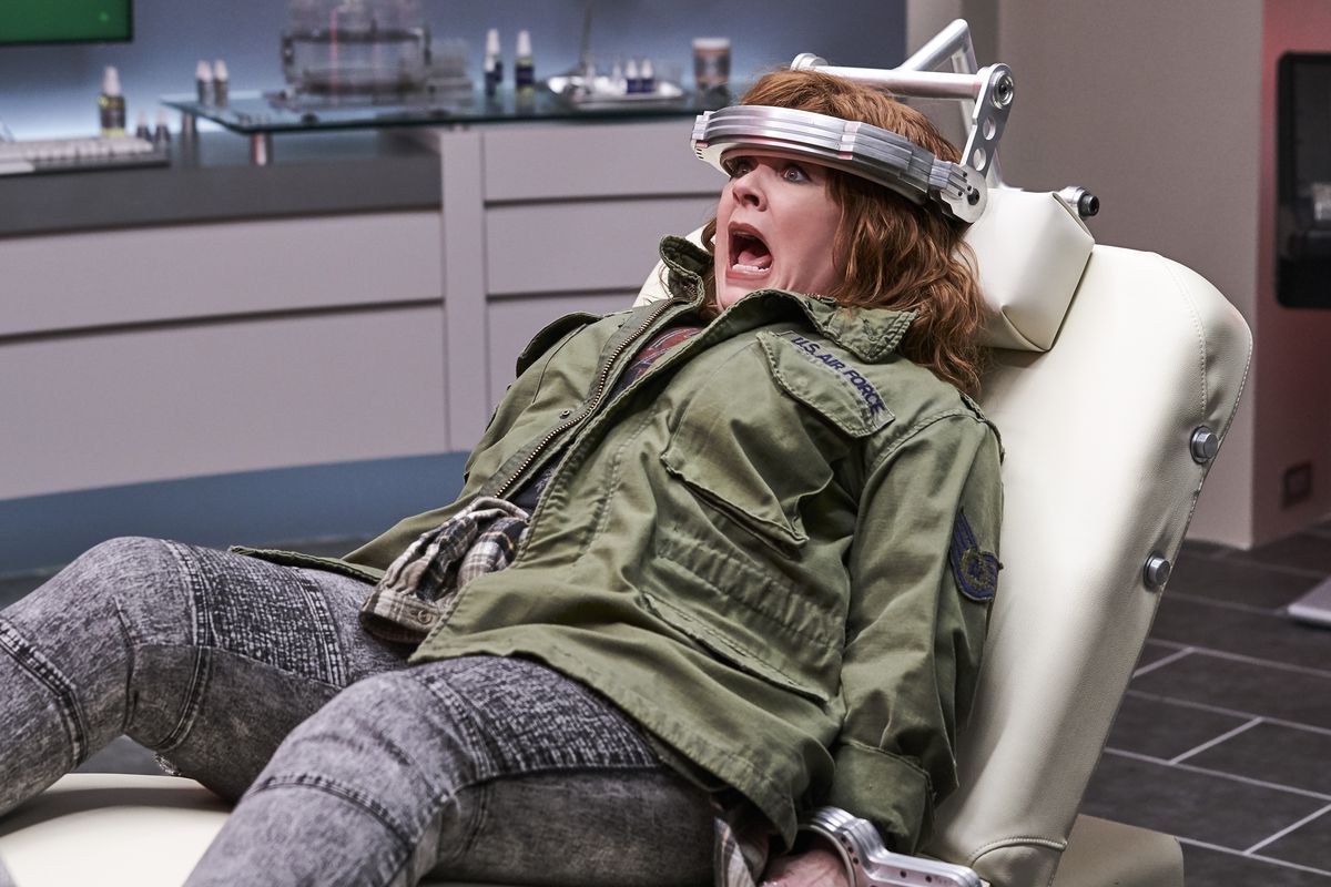 Melissa McCarthy, legata a una sedia futuristica con una fascia di metallo intorno alla testa, urla scioccata in Thunder Force