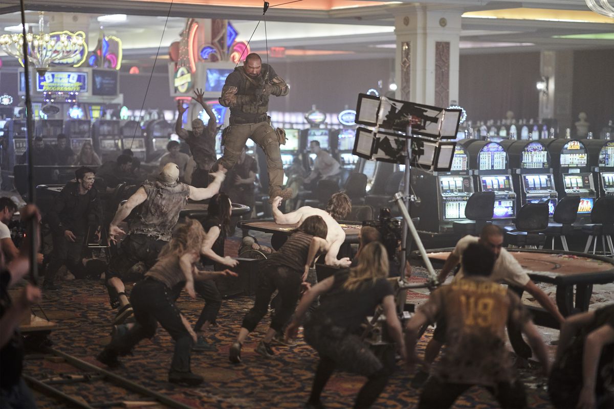 Dave Bautista, su una piattaforma di cablaggio, corre sui tavoli di un casinò mentre attori che interpretano gli zombi lo inseguono in un'immagine dietro le quinte di Army of the Dead