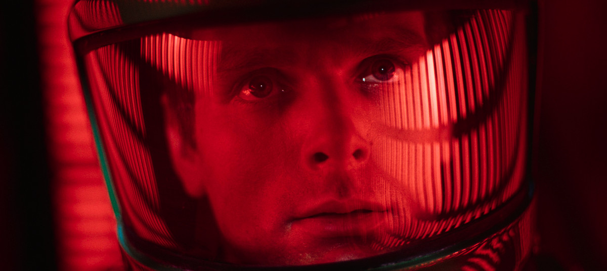 Un uomo con un casco spaziale fissa file di colonne di luce illuminate di rosso.