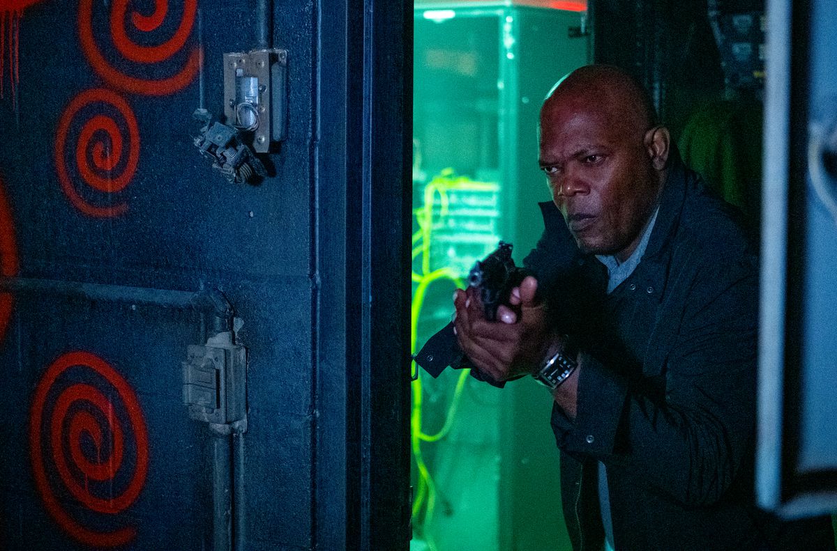 Samuel L. Jackson, con la pistola in mano, guarda in una stanza con spirali dipinte di rosso sulle pareti