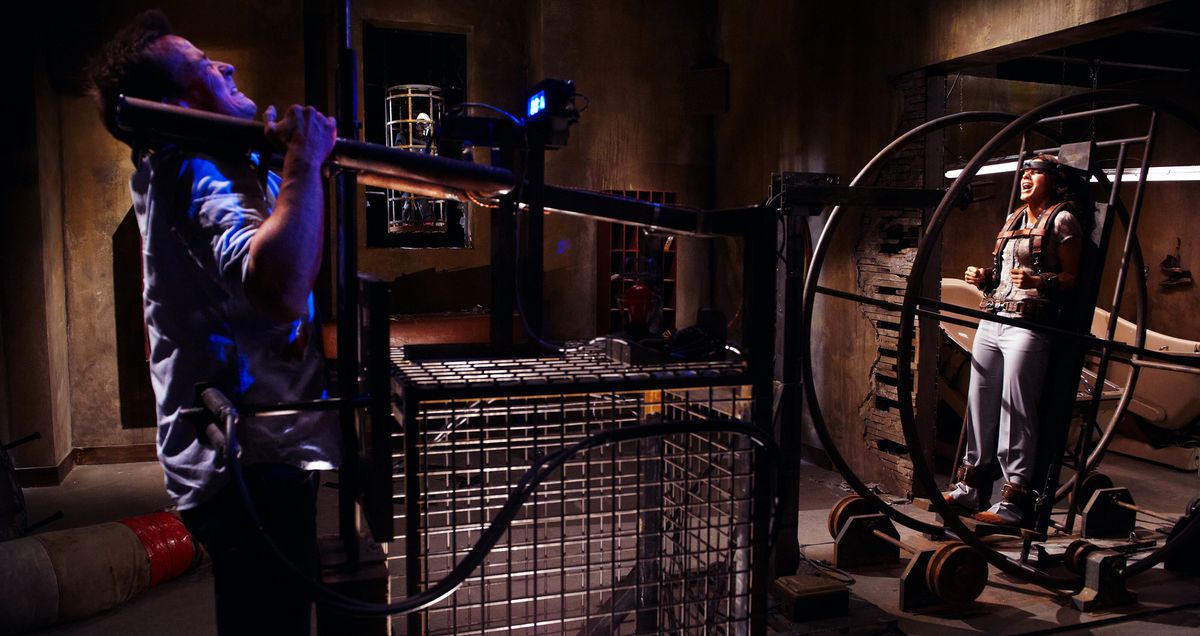 A man heaves on an elaborate machine as a woman screams from a different part of the machine in Saw 3D