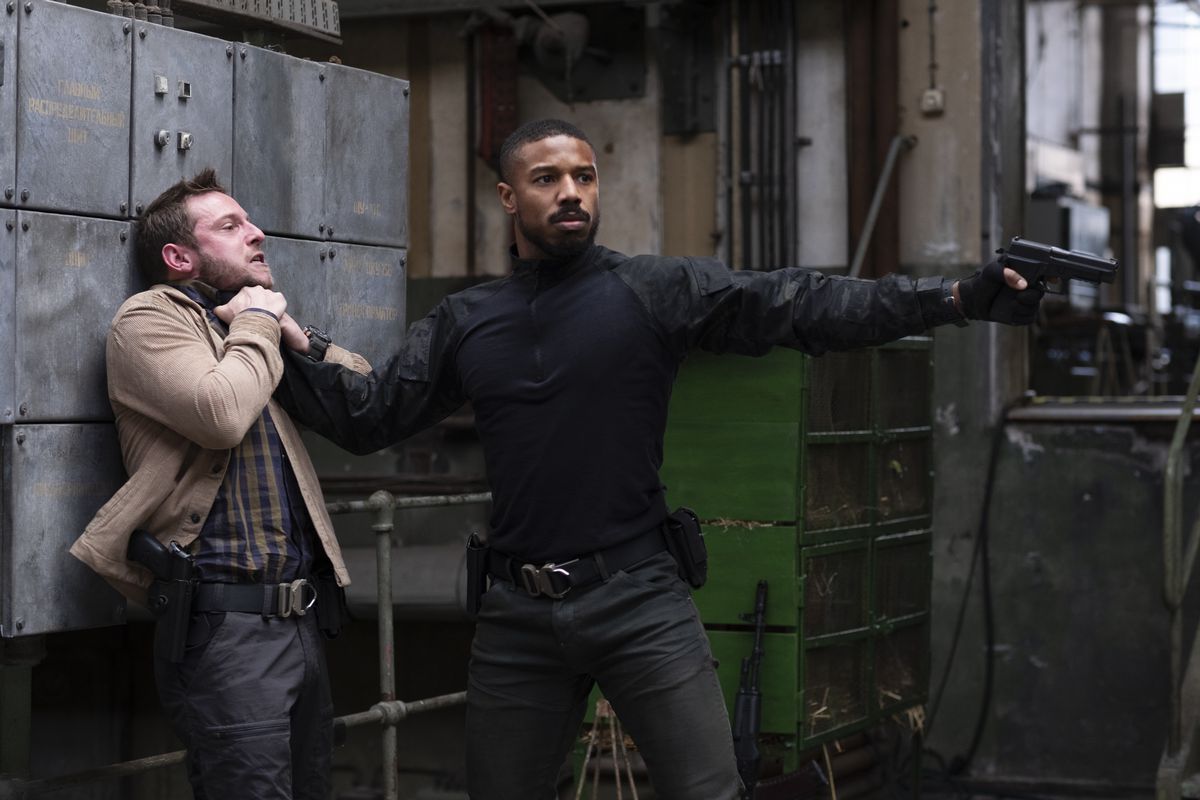 Michael B. Jordan holds a man by his throat while point a pistol off-screen.