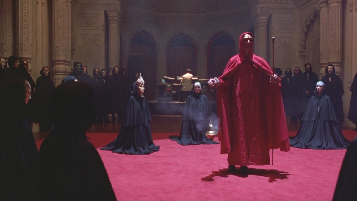 Un cerchio di figure mascherate, una vestita di rosso e le altre in nero, le circondava.