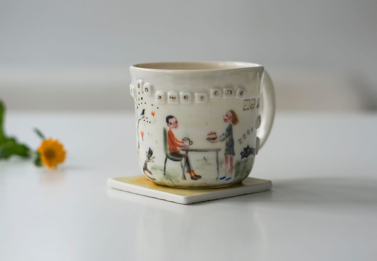 Una tazza di ceramica con una scena piacevole.  Le tessere di Scrabble scorrono lungo il bordo.