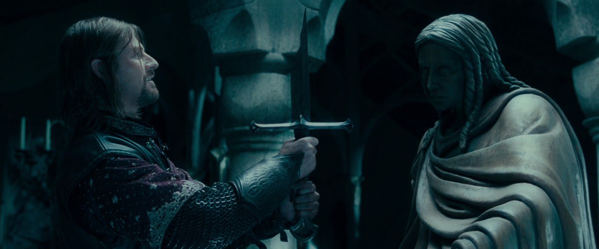 Sean Bean mentre Boromir solleva la spada spezzata Narsil con un leggero sorriso in La Compagnia dell'Anello
