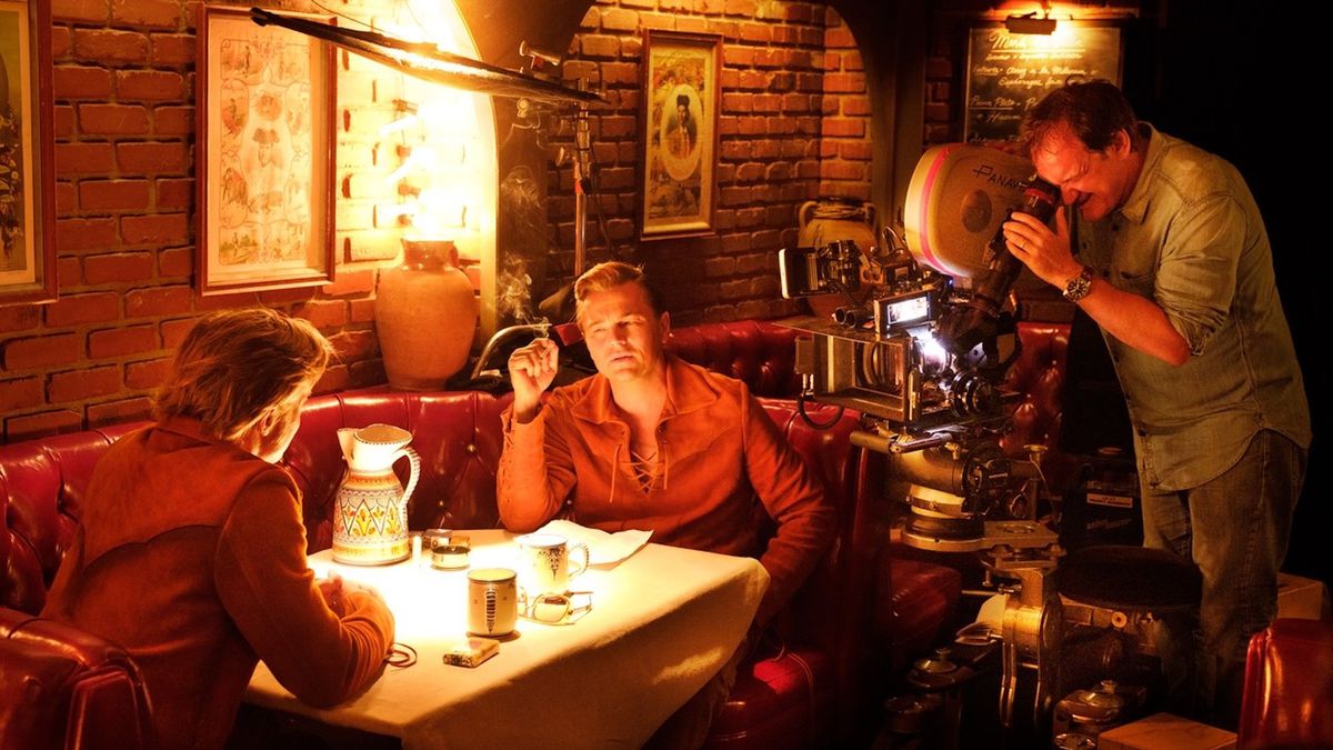 Brad Pitt e Leonardo DiCaprio siedono l'uno di fronte all'altro in uno stand di un ristorante mentre Quentin Tarantino guarda da dietro la telecamera le riprese di C'era una volta ... a Hollywood