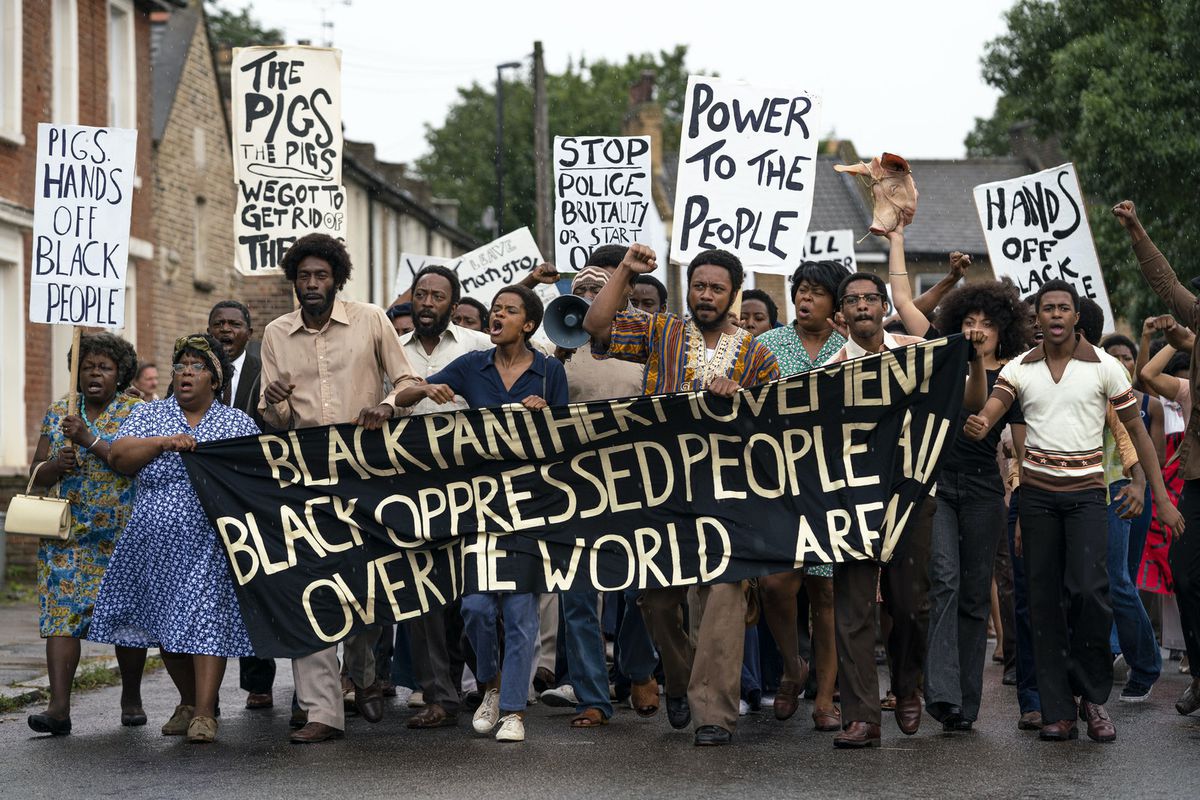 Un folto gruppo di manifestanti neri porta uno striscione della Pantera Nera nel film della serie Small Axe di Steve McQueen Mangrove