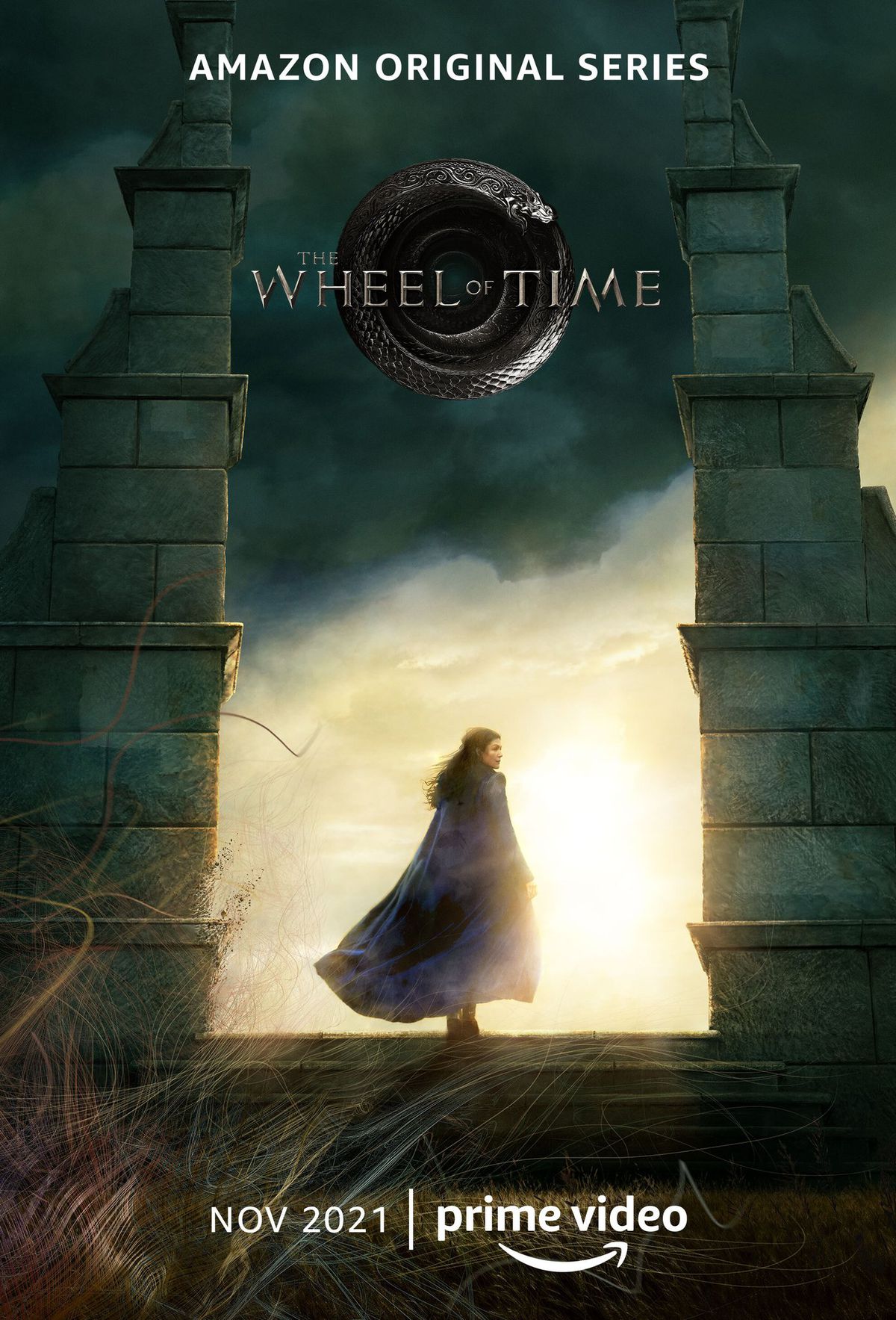 Rosamunde Pike mentre Moiraine attraversa due pilastri di pietra in un poster per la serie originale di Amazon The Wheel of Time. 