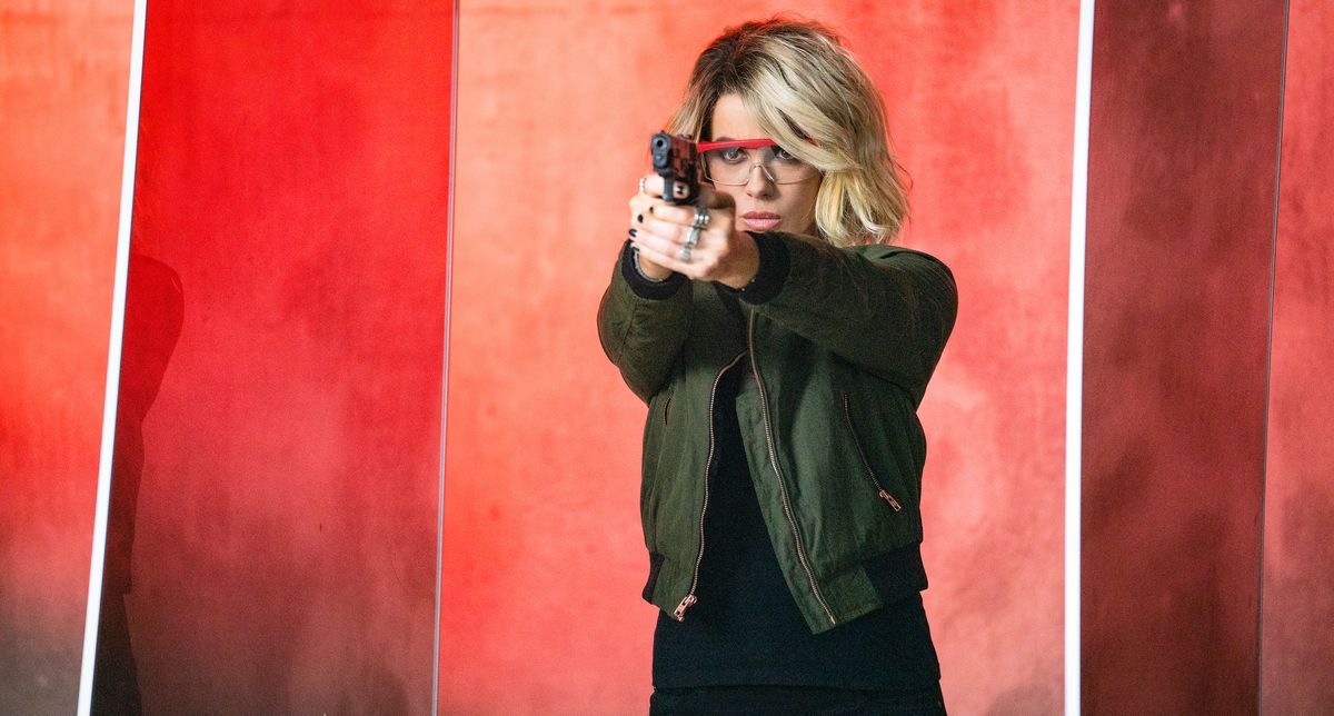 Kate Beckinsale spara con una pistola davanti a uno sfondo arancione e rosso vivo in Jolt