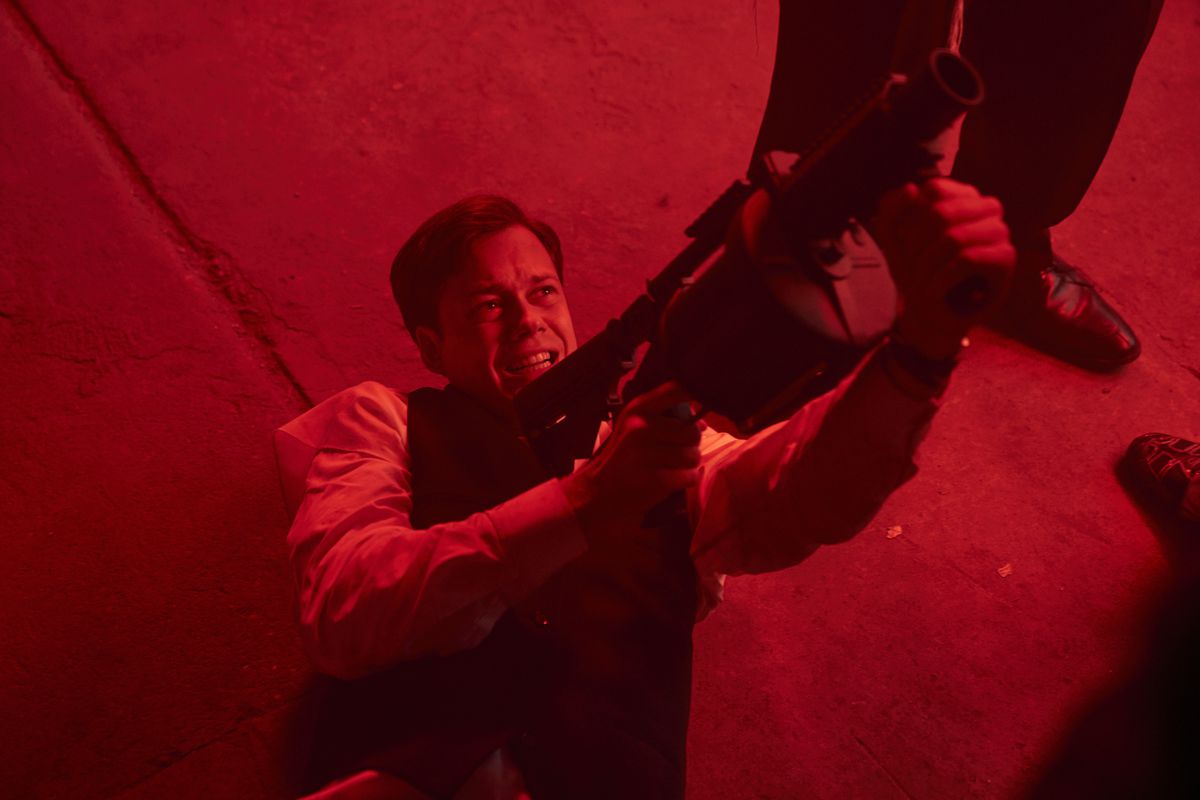 Un uomo sulla schiena in uno spazio illuminato di rosso, fa una smorfia e punta un'enorme arma da proiettile verso il cielo in Naked Singularity