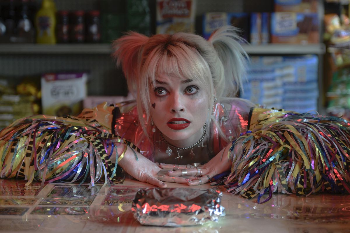 Margot Robbie appoggia le braccia su un bancone di gastronomia e guarda supplichevole il suo panino per la colazione nei panni di Harley Quinn in Birds of Prey.