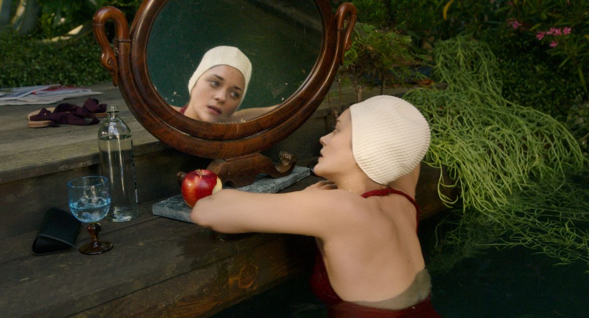 Marion Cotillard, in costume da bagno e cuffia bianca, si esamina in uno specchio rotondo in Annette