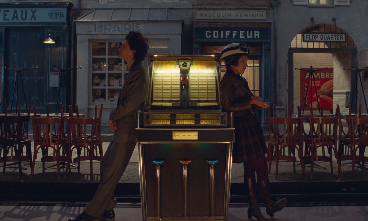 Timothée Chalamet e Lyna Khoudri si appoggiano ai lati opposti di un jukebox all'aperto (è una cosa?), l'uno di fronte all'altra in The French Dispatch di Wes Anderson.