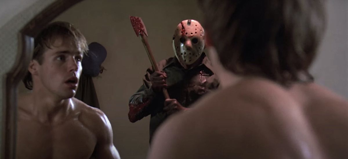 A shirtless young man looking at himself in the mirror sees hockey-masked killer Jason Voorhees coming up behind him with a bloody axe in Friday The 13th Part V: A New Beginning