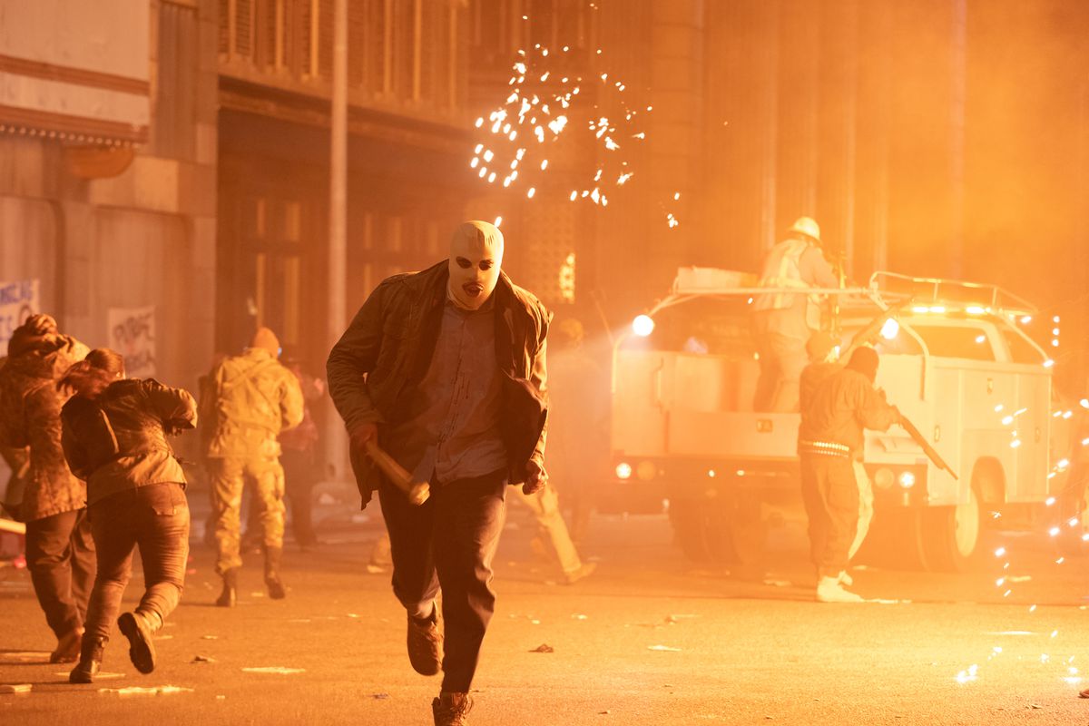 A masked purger runs from an explosion in The Forever Purge