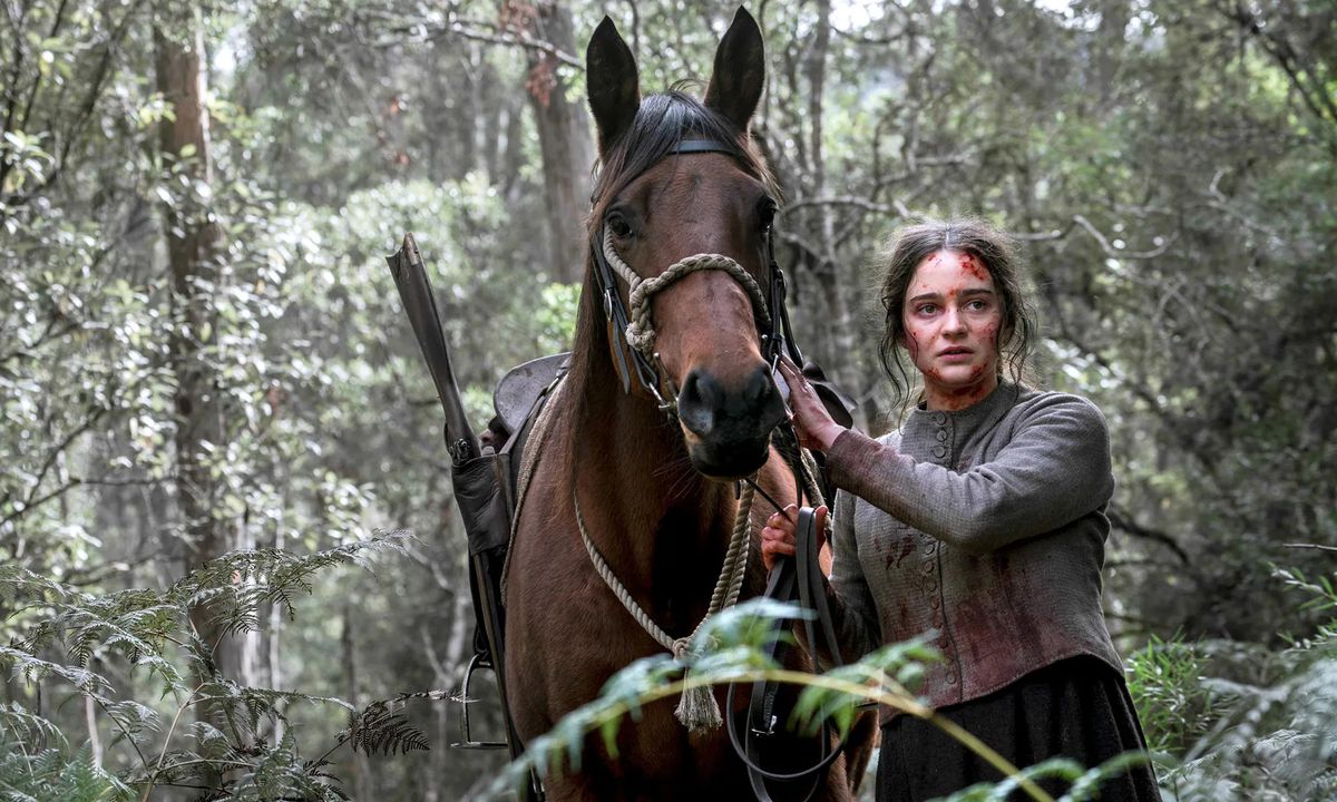 Clare (Aisling Franciosi) insanguinata e cammina attraverso una foresta con un cavallo in The Nightingale.