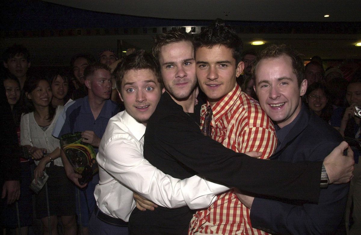 Elijah Wood, Dominic Monaghan, Orlando Bloom, and Billy Boyd embracing on the red carpet at the Sydney premiere of The Lord of the Rings: The Fellowship of the Ring