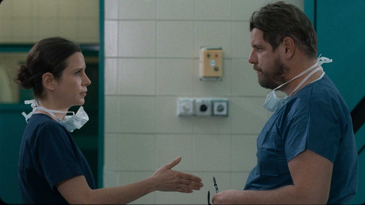 Natasa Stork, in scrubs at a hospital, extends a hand to a similarly dressed man in Preparations to be Together for an Unknown Period of Time