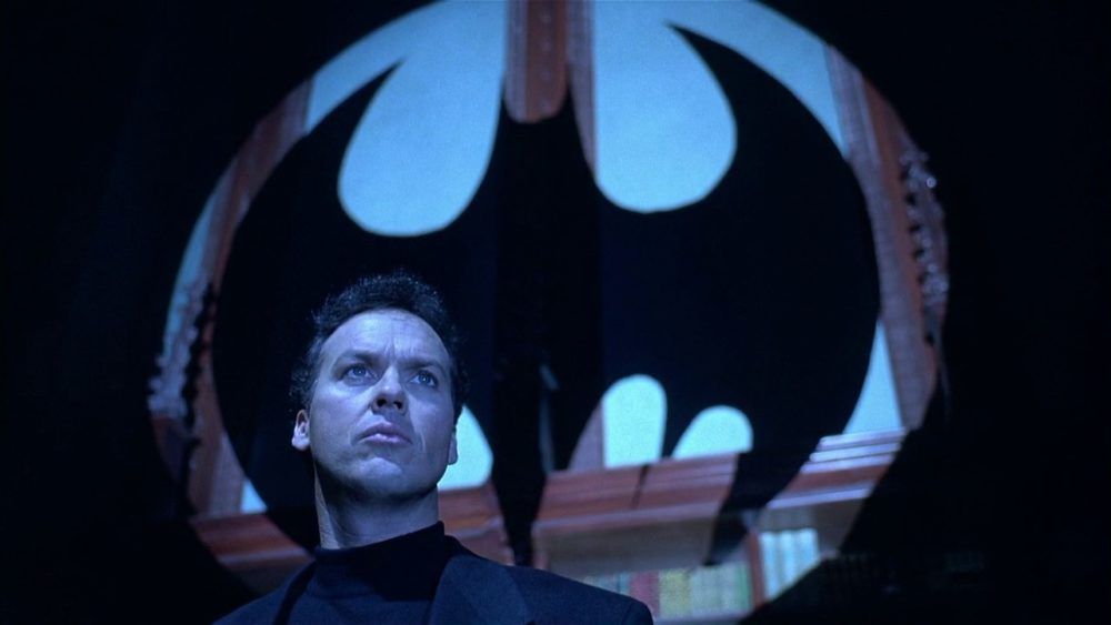 Bruce Wayne (Michael Keaton) in piedi di fronte a una sagoma del segnale del pipistrello in Batman Returns.