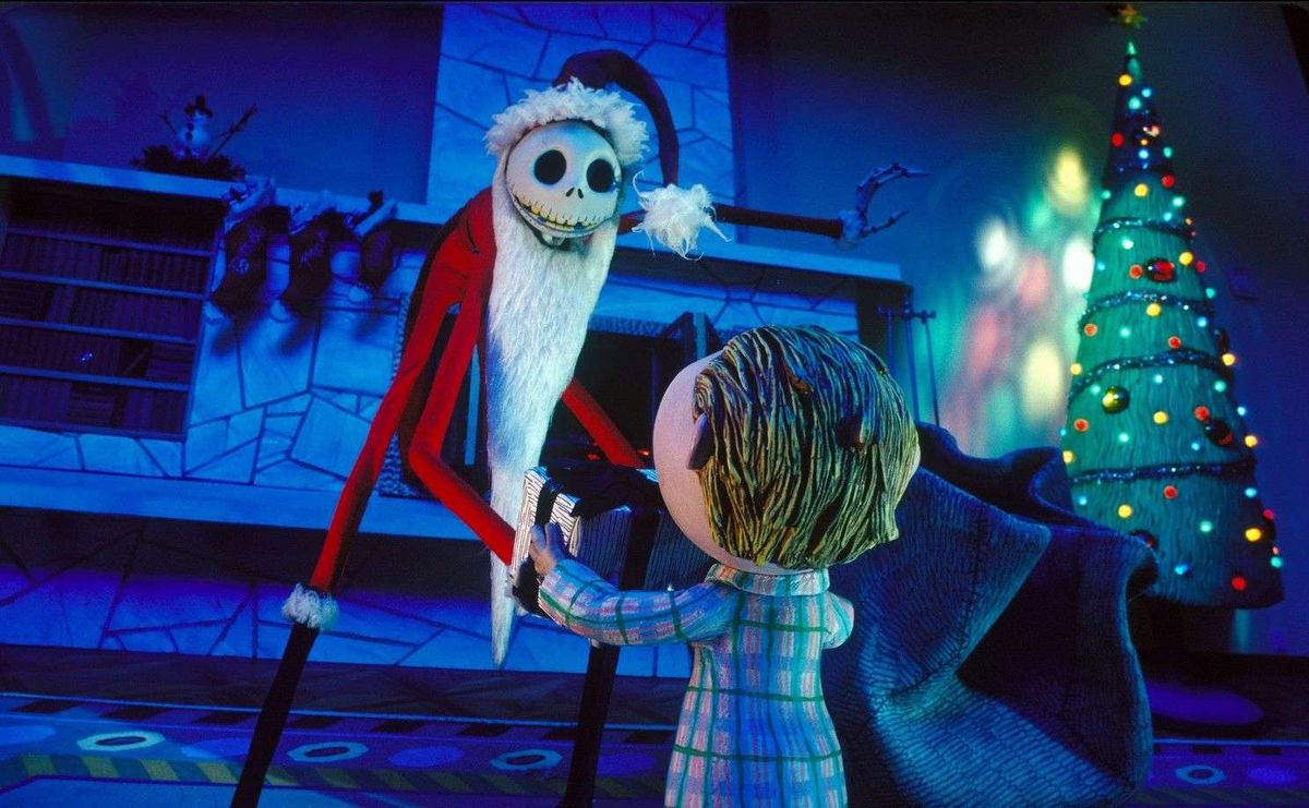 Un'alta figura simile a uno scheletro con un vestito da Babbo Natale s'inchina davanti a un ragazzo in un soggiorno con un albero di Natale sullo sfondo.