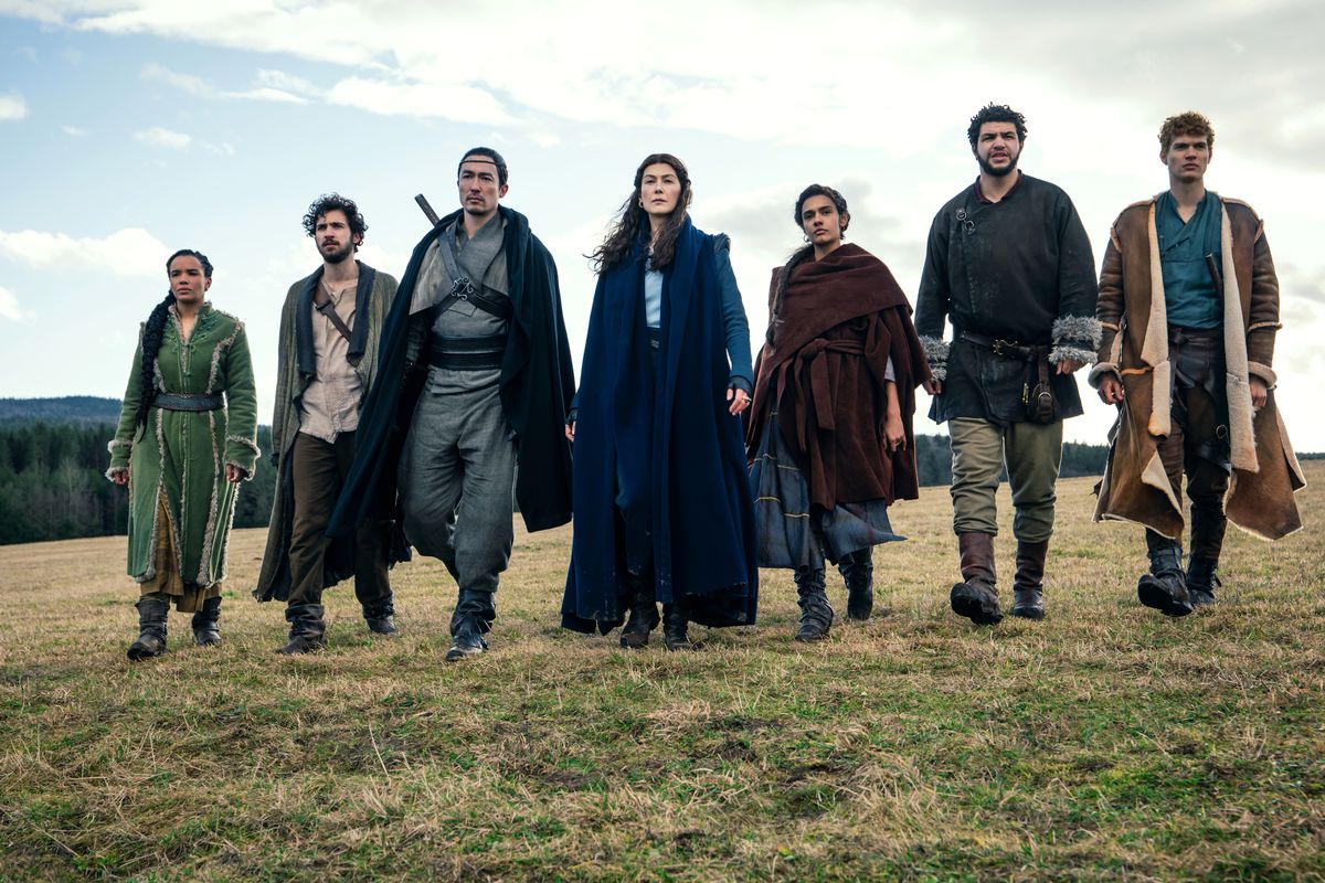 the core Wheel of Time cast — Nynaeve, Mat, Lan, Moiraine, Egwene, Perrin, and Rand — walking across a field