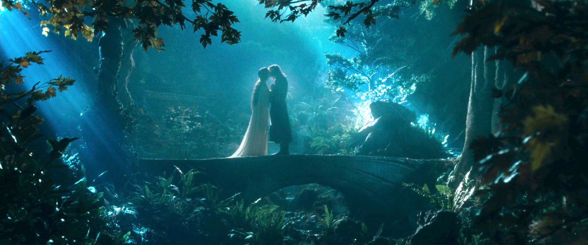 Arwen and Aragorn kiss on a bridge in Rivendell in The Fellowship of the Ring. She is wearing a white dress with a flowing train.