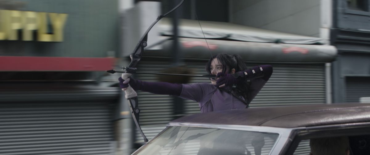Kate Bishop si blocca dal finestrino di un'auto per scoccare una freccia contro un inseguitore durante un inseguimento in auto a Occhio di Falco