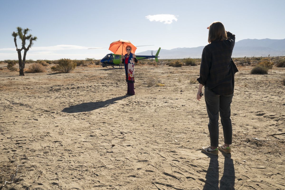 Jean Smart as Deborah Vance carrying an orange umbrella and walking toward a helicopter in the Las Vegas desert. She’s turning and smiling at Ava (not pictured).