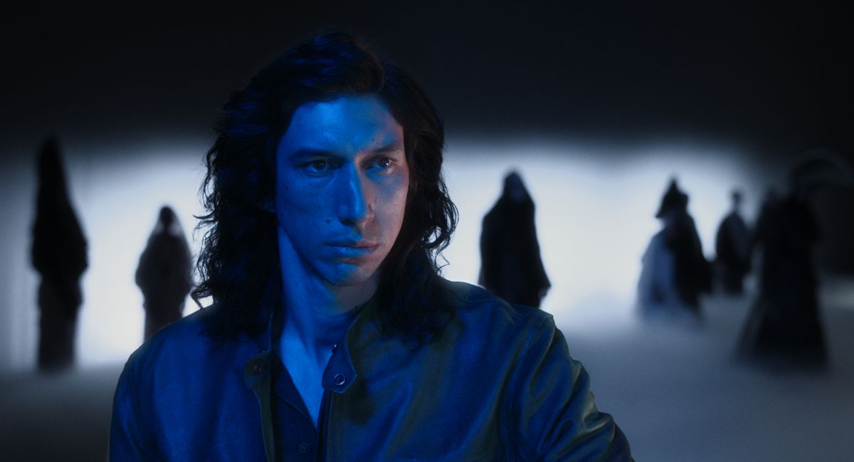Adam Driver, in dim blue light with fog and tree shapes behind him, in Annette