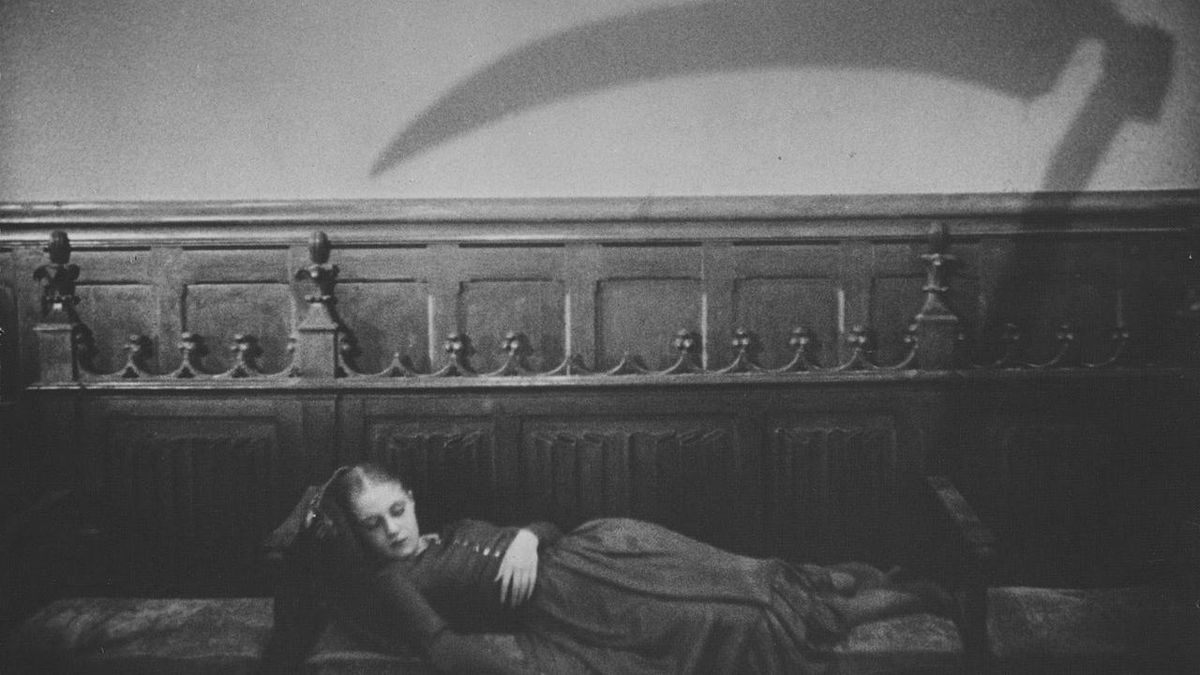 Rena Mandel priva di sensi su un divano con l'ombra della falce che incombe in alto in Vampyr (1932)