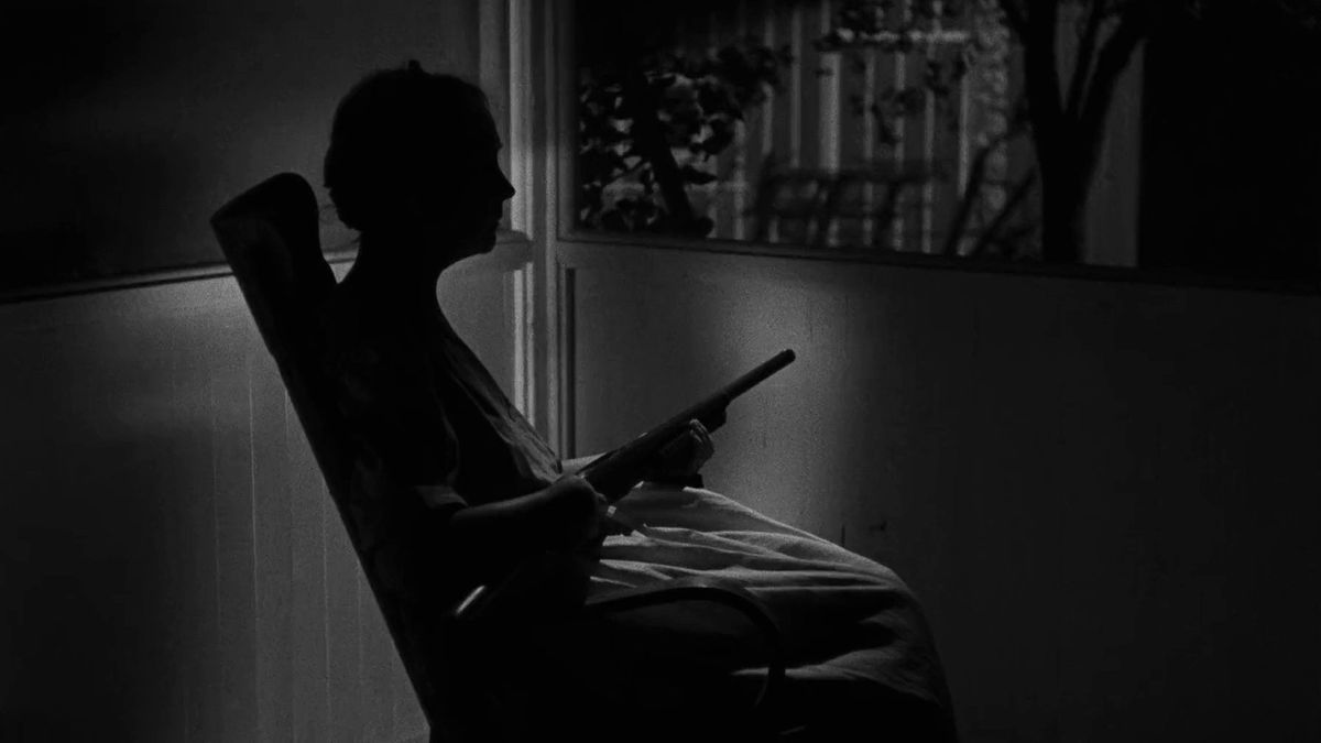 Lillian Gish nei panni di Rachel Cooper in attesa su una sedia a dondolo con in mano un fucile in La notte del cacciatore.
