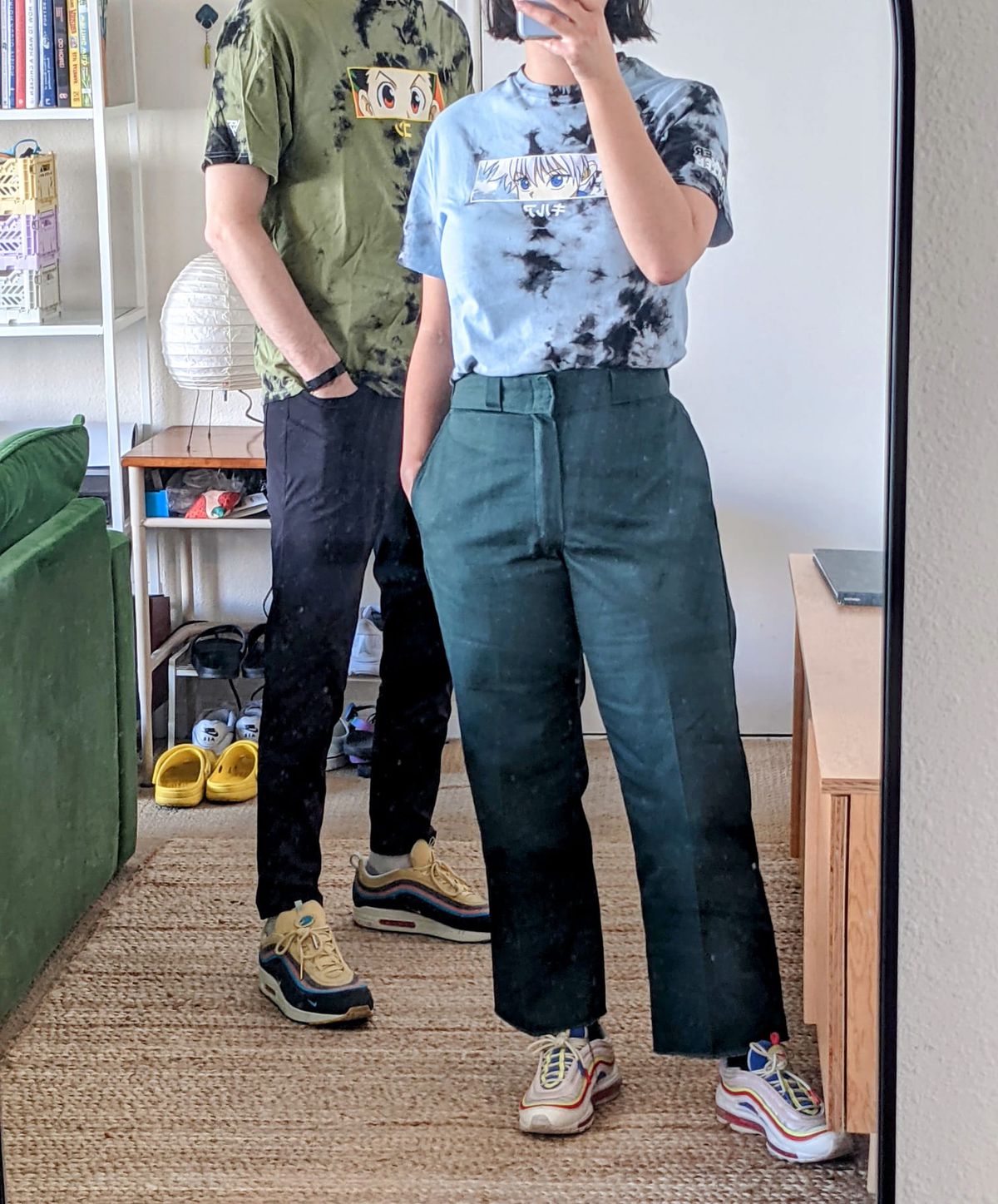 due persone in piedi che si fanno un selfie allo specchio.  uno indossa una maglietta kilua e uno indossa una maglietta gon.  sono entrambi tie-dye. 