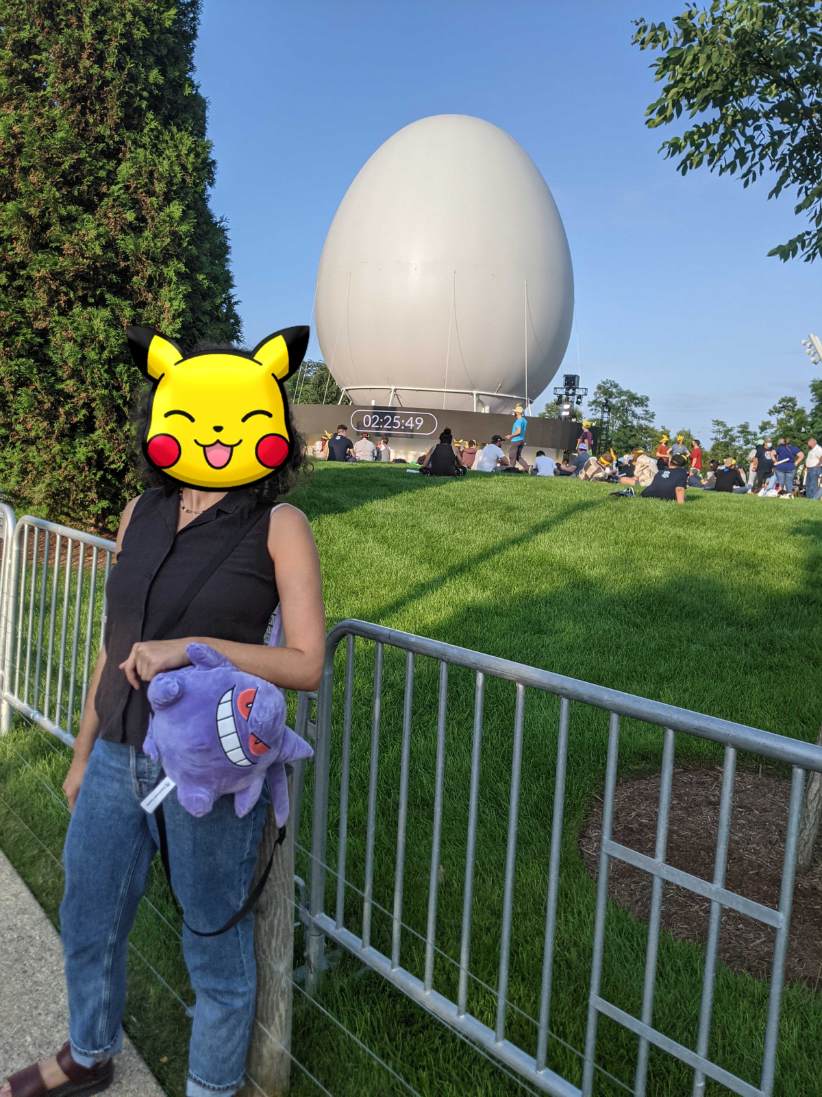una persona in piedi al pokemon go fest che indossa uno zaino gengar.  la sua faccia è bloccata da pikachu.