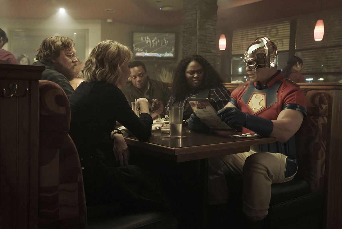 L'intero team di Peacemaker seduto in uno stand in un ristorante di famiglia in un fermo immagine dell'episodio 1