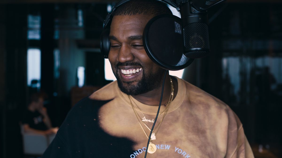un'immagine dal terzo episodio di jeen-yuhs: A Kanye Trilogy di un Kanye West in cuffia sorridente in uno studio di registrazione, con un microfono e un filtro anti-pop davanti al viso
