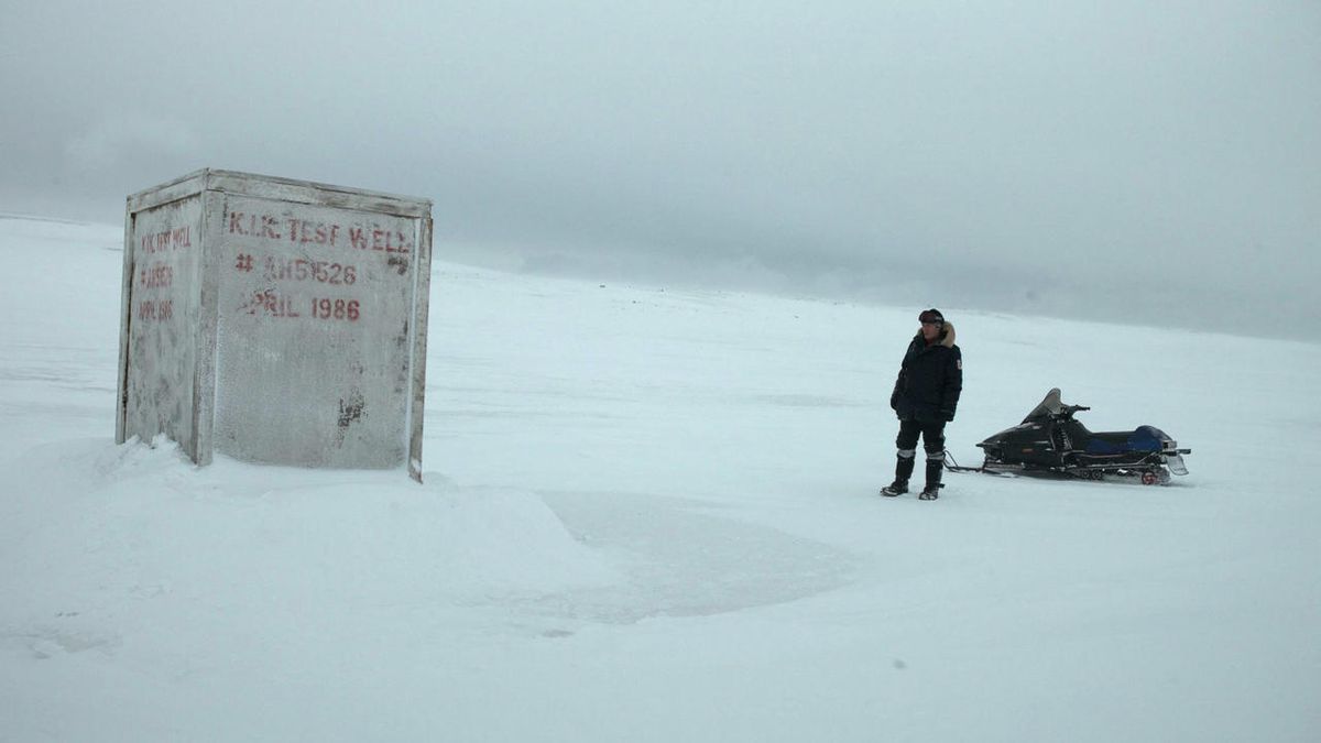Un uomo in piedi davanti a un contenitore bianco nel mezzo della tundra antartica in The Last Winter.