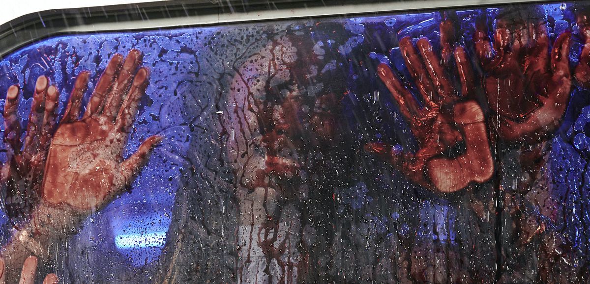 Una faccia insanguinata e quattro mani insanguinate premono contro l'interno di un finestrino di un'auto incredibilmente insanguinato nel massacro della motosega del Texas del 2022