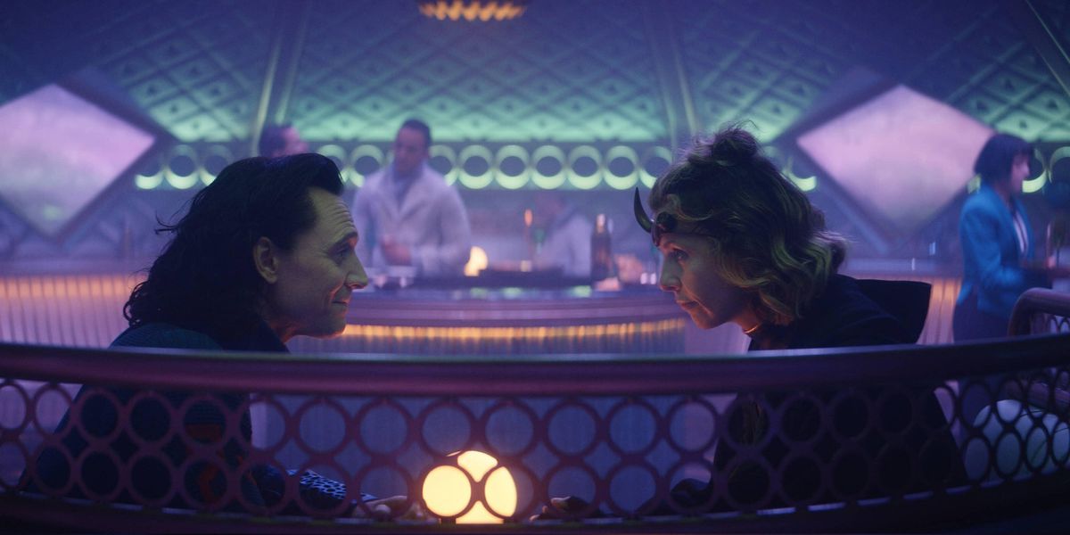 Tom Hiddleston e Sophia Di Martino nei panni di Loki e Sylvie in un bar del treno insieme a Loki, con luci blu, rosa e viola