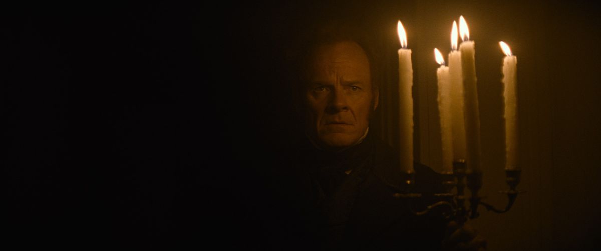 Alistair Petrie in una stanza incredibilmente buia in The Cursed, illuminata solo dal candelabro che tiene in mano
