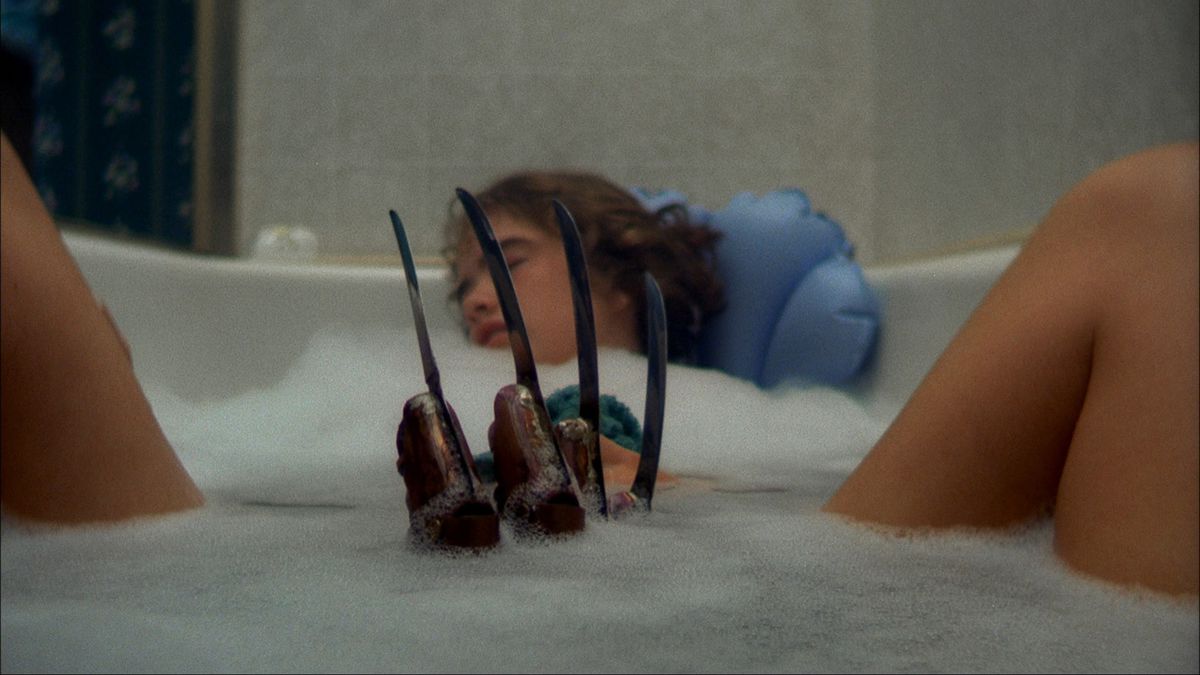 Un guanto artigliato si allunga dalle acque di una vasca da bagno verso una donna addormentata in A Nightmare on Elm Street.