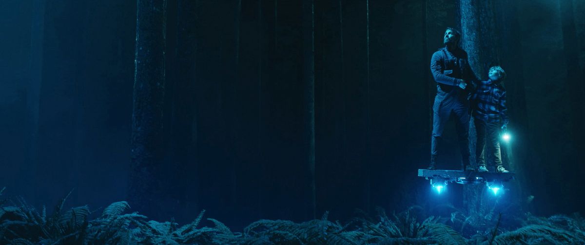 Il giovane Adam e Big Adam (Ryan Reynolds) navigano in una foresta blu scuro su una piattaforma volante luminosa in The Adam Project