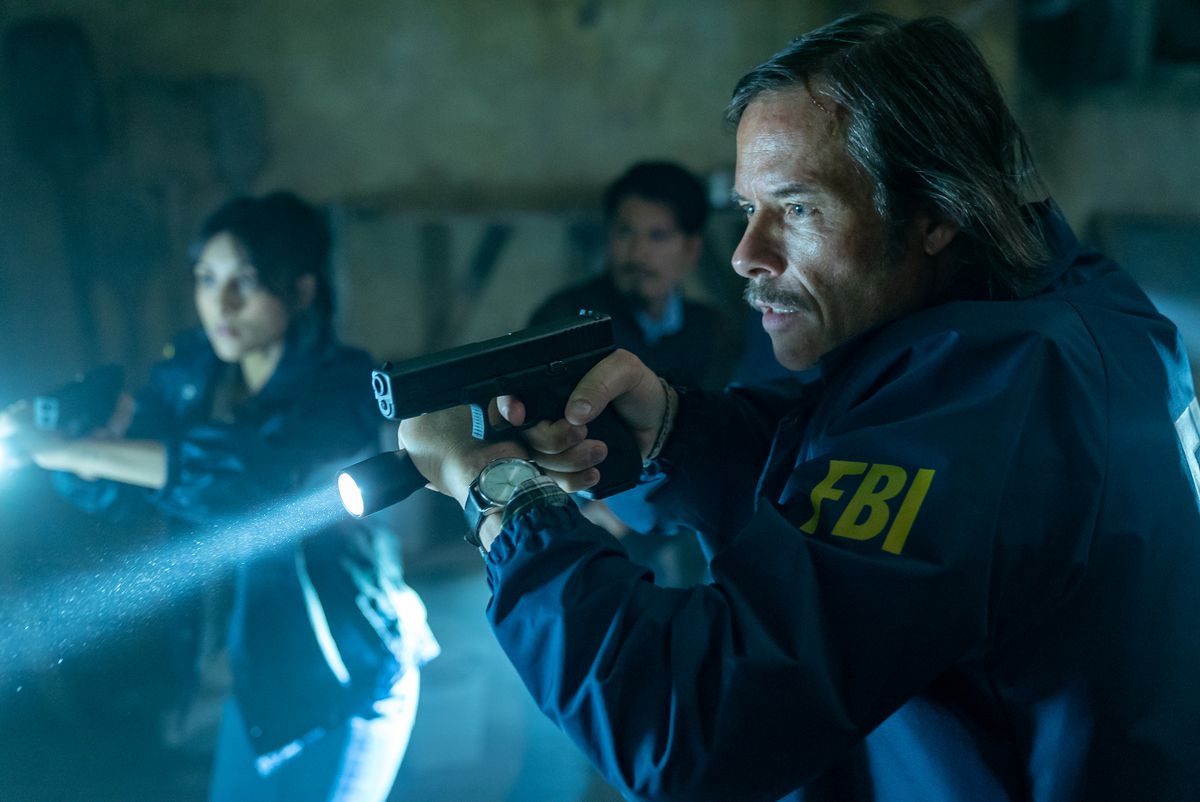 Guy Pearce con una giacca dell'FBI brandisce una pistola e una torcia nel film Memory.