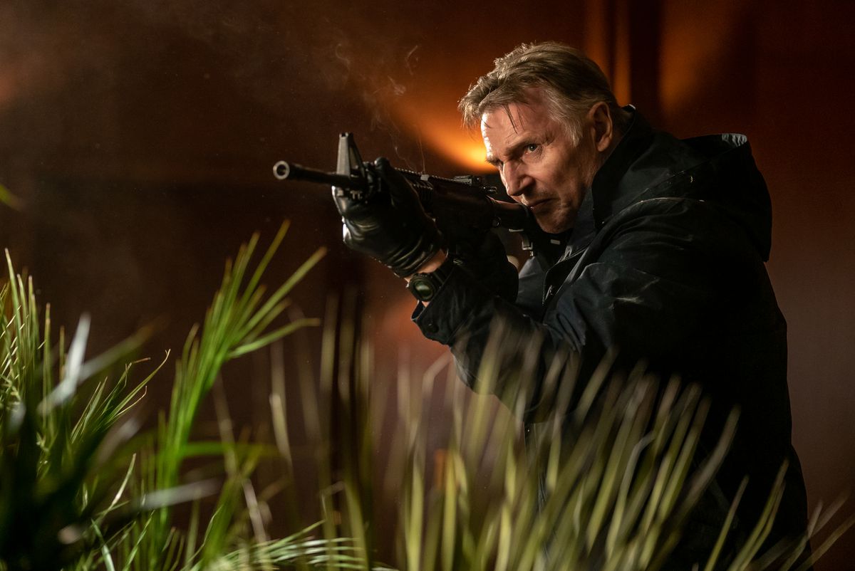 Liam Neeson cammina nell'erba alta con un fucile d'assalto in Memory